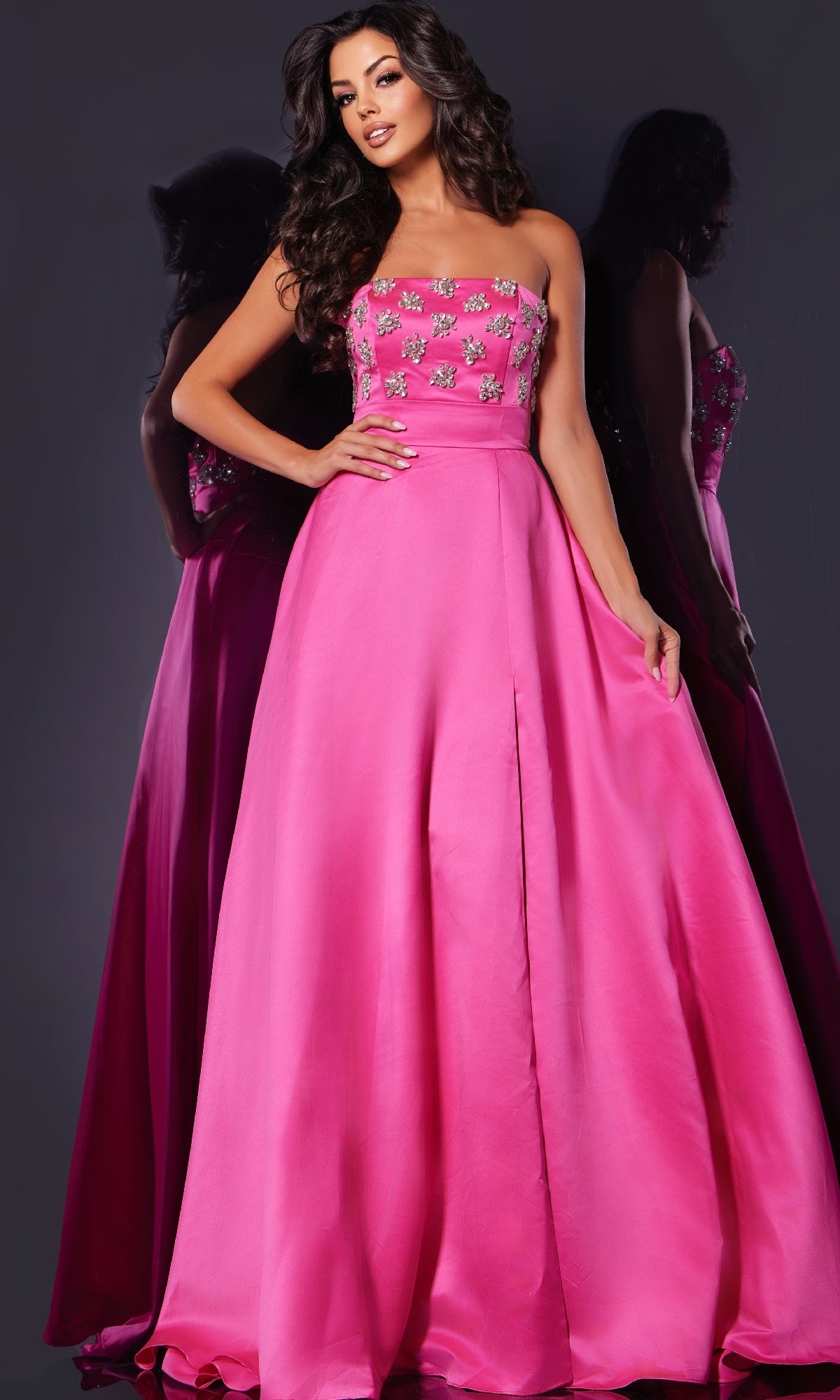 A woman stands against a dark background in the Jovani 43822 long prom dress—a strapless, floor-length pink gown with an A-line skirt, jewel-embellished bodice, and delicate floral details.
